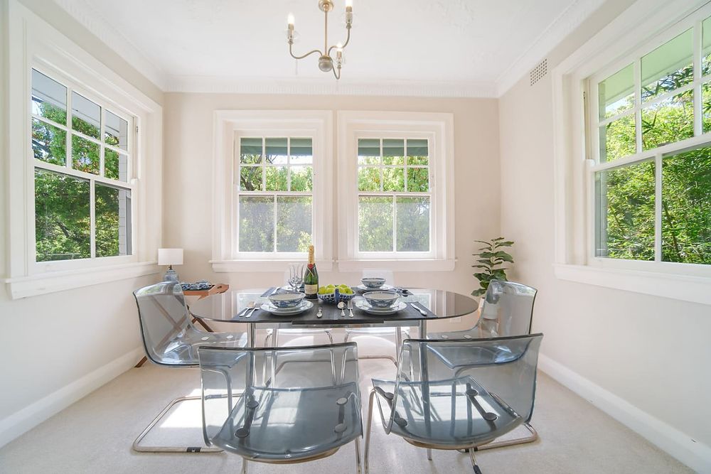 Dining table with a glass top and clear chairs beside two windows